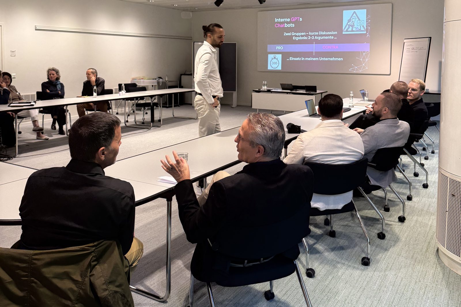 Speaker standing in the middle of the room discussing with participants at a U-shaped table